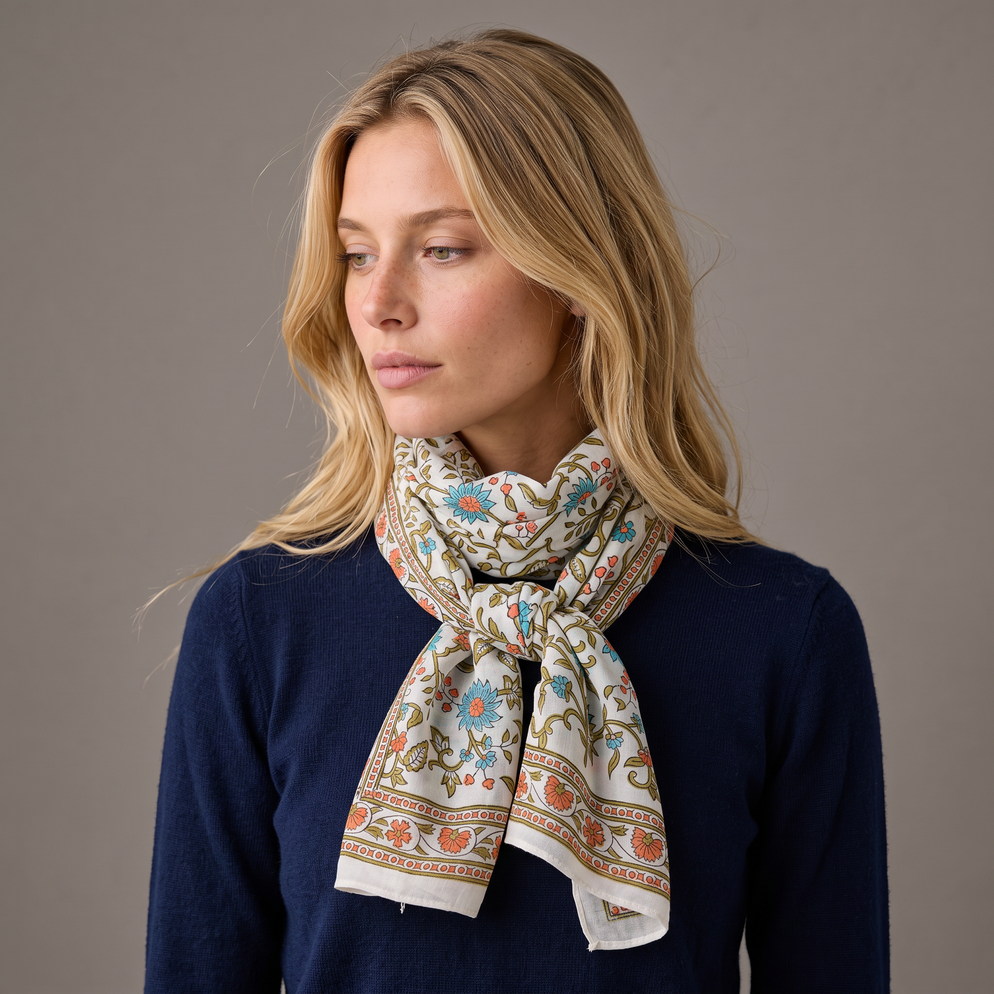Foulard Vatika porté : noué au cou sur un pull marine, lianes fleuries sur fond blanc