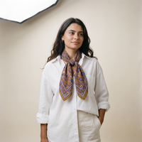 Foulard Sona porté : noué au cou sur une chemise blanche, fleurs violettes sur ocre
