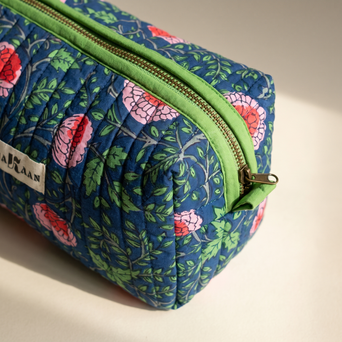 Détail de la trousse Jaya : matelassage vertical, zip et ruban de coton vert