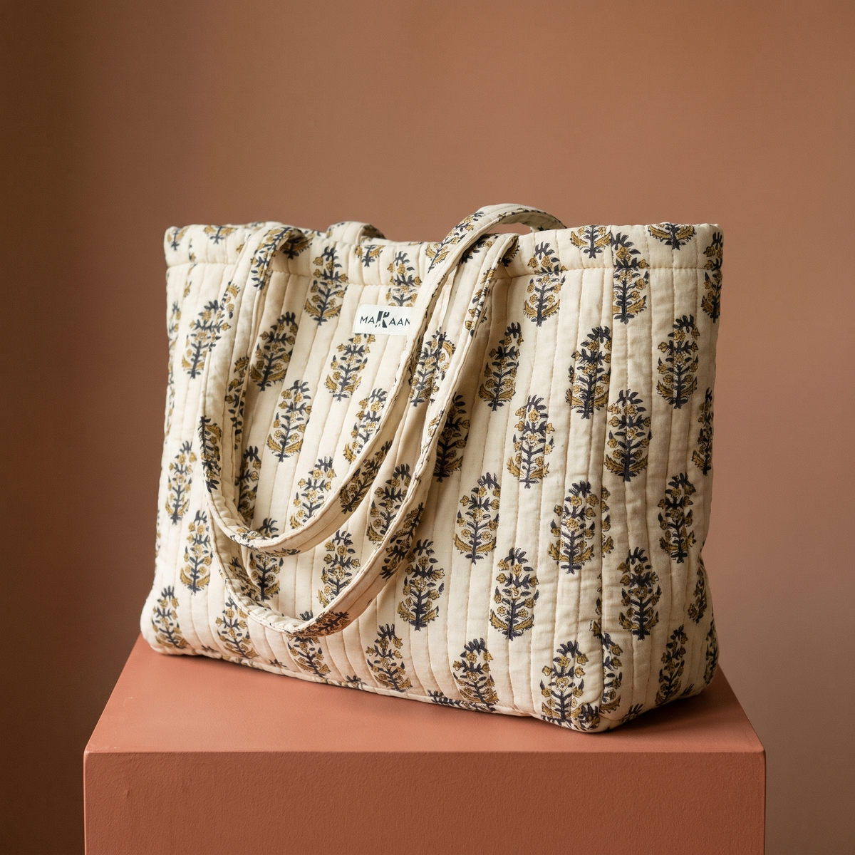 Cabas Chandan en coton matelassé : grand sac blockprint à buti noir et miel sur écru, deux anses en tissu imprimé, posé sur un socle