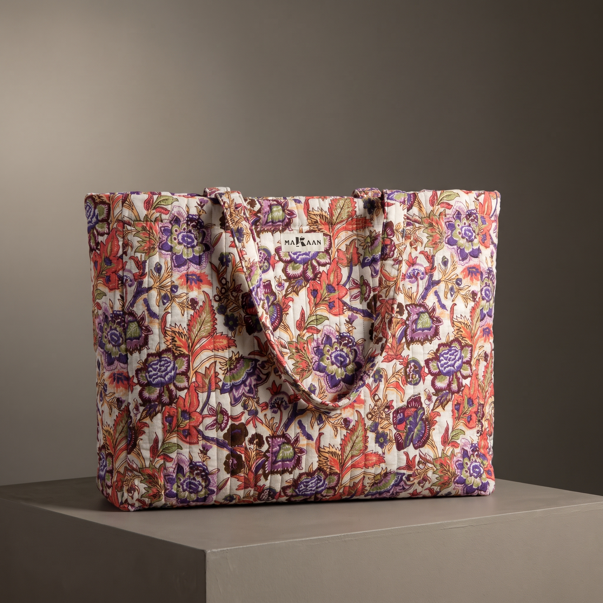 Cabas Gulzar en coton matelassé : grand sac blockprint à jardin prune et corail sur crème, deux anses en tissu imprimé, posé sur un socle