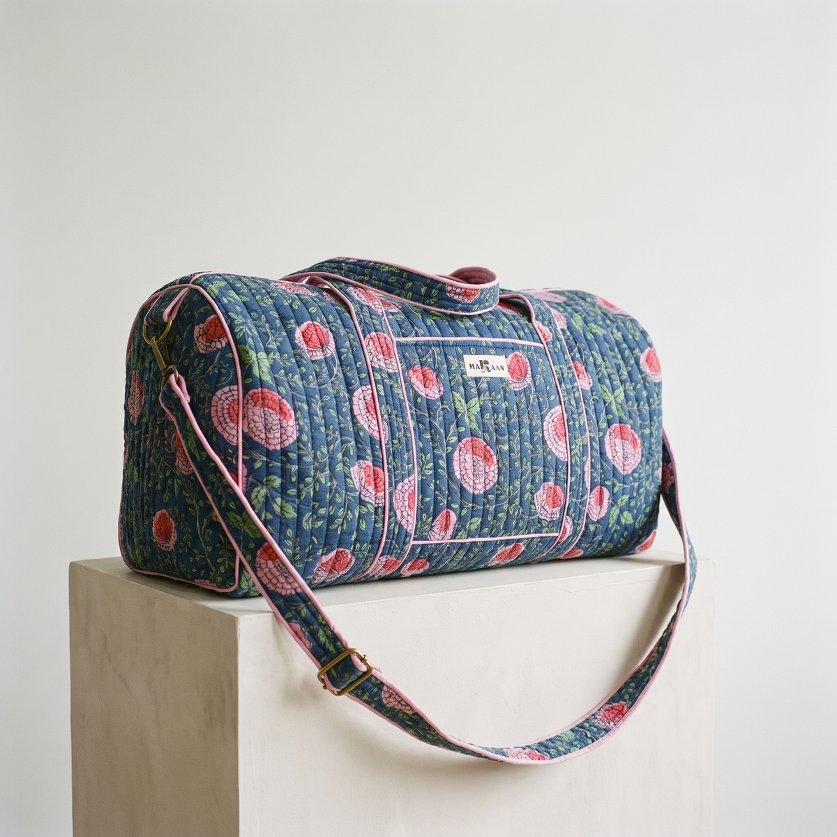 Sac week-end Kusum : polochon en coton matelassé blockprint, fleurs roses et corail sur indigo, biais rose, posé sur un socle clair