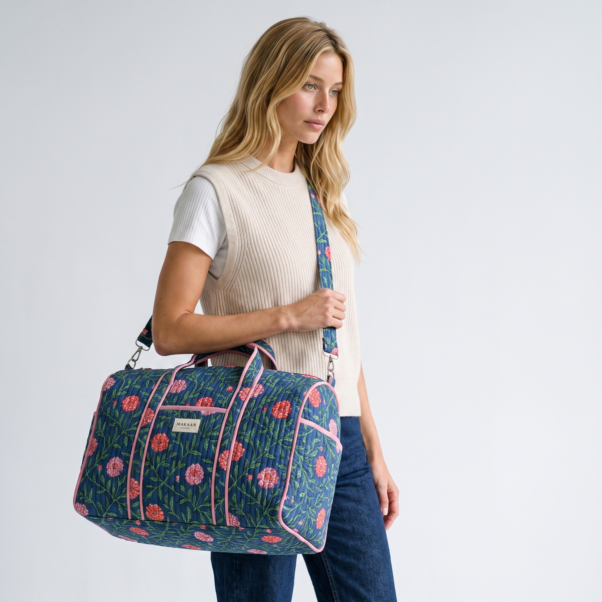 Sac week-end Kusum porté à l’épaule par sa bandoulière réglable, sur un gilet de maille écrue et un jean brut