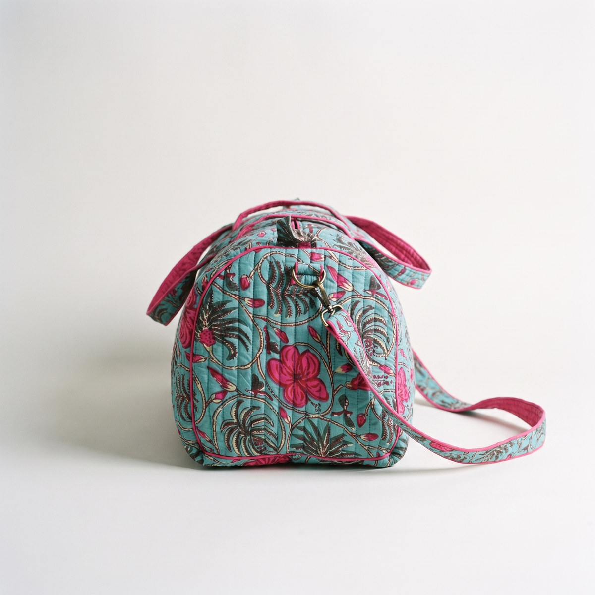 Sac week-end Nilofar vu de bout : panneau latéral arrondi bordé de fuchsia, boucle en laiton de la bandoulière