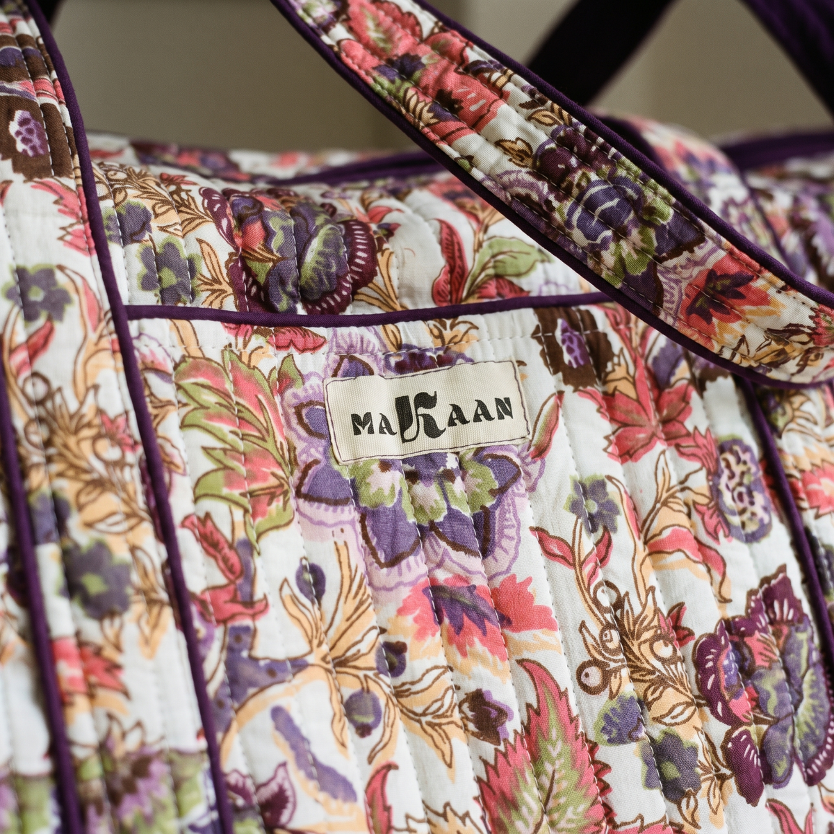 Détail du sac week-end Ketaki : blockprint crème, fleurs prune et frondes ocre, étiquette MAKAAN et biais prune