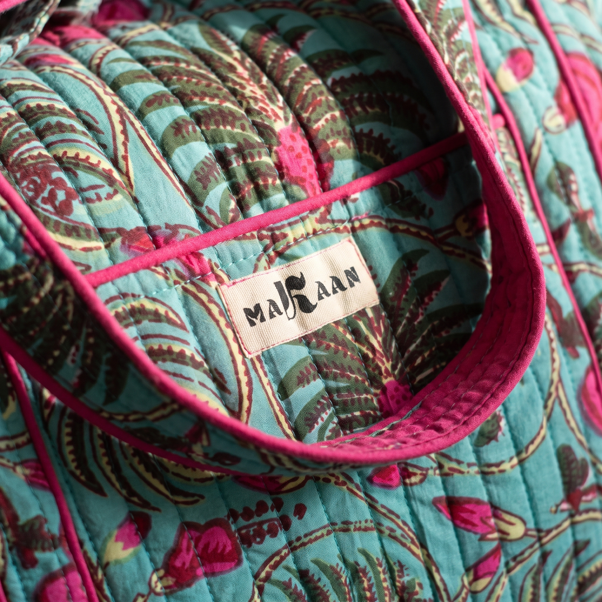 Détail du sac week-end Nilofar : blockprint turquoise et fougères, étiquette MAKAAN sur la poche, biais fuchsia
