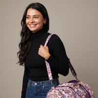 Femme souriante portant le sac week-end Ketaki en bandoulière, floral prune et corail sur crème