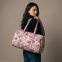 Sac week-end Ketaki porté à l’épaule par ses anses, vue de trois-quarts dos, jardin prune et corail sur coton crème