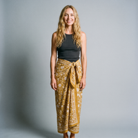 Femme souriante portant le paréo Haldi noué à la taille, blockprint crème réservé sur jaune curcuma