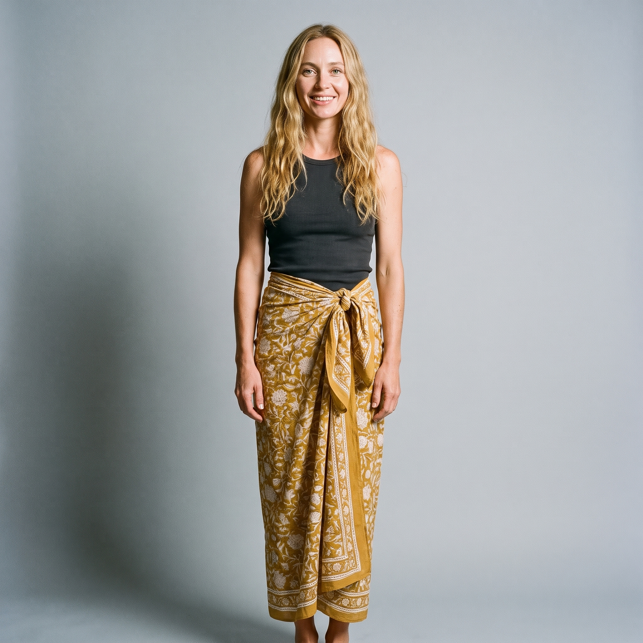 Femme souriante portant le paréo Haldi noué à la taille, blockprint crème réservé sur jaune curcuma