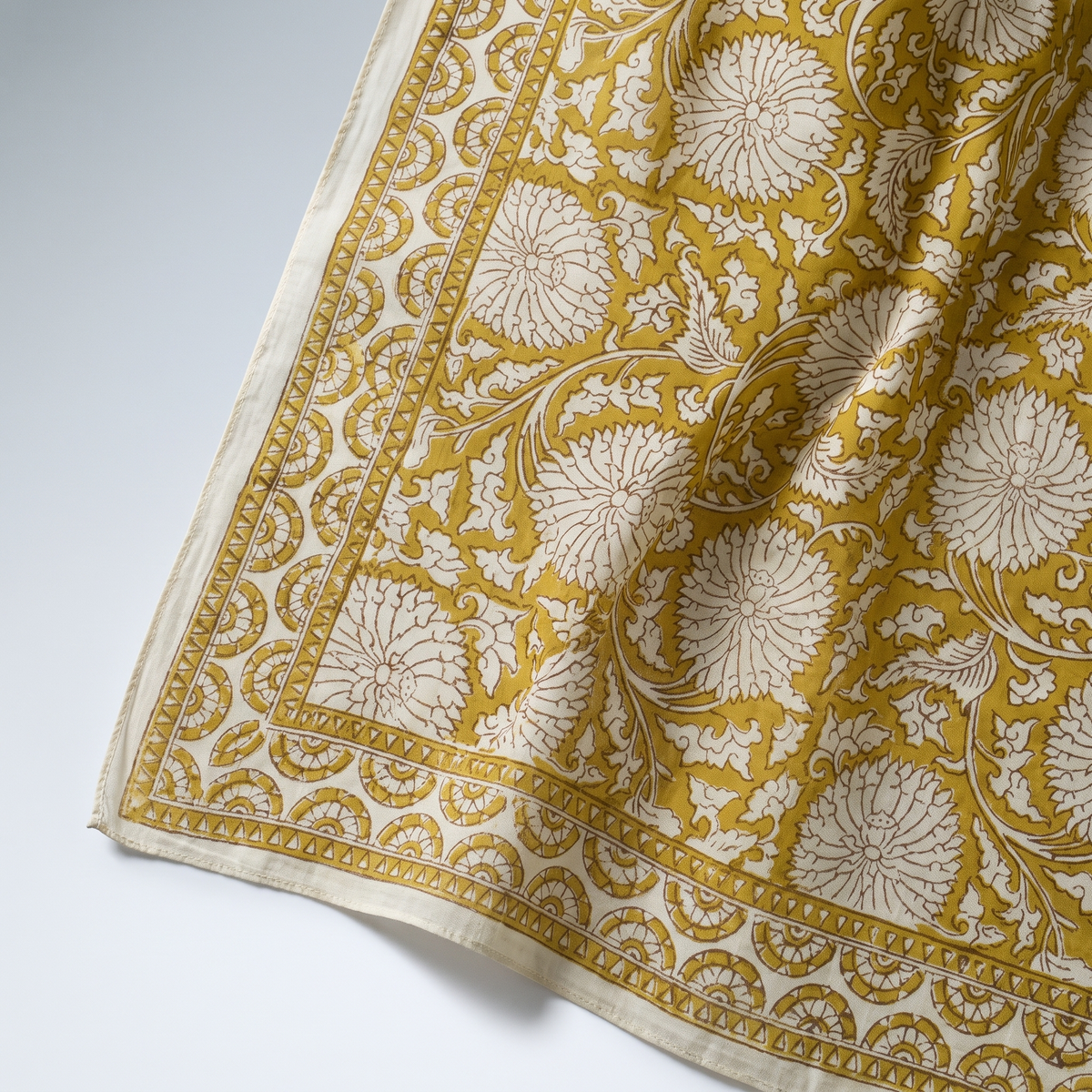 Détail du blockprint du paréo Haldi : fleurons crème réservés dans le jaune curcuma, bordure à dents et liseré écru