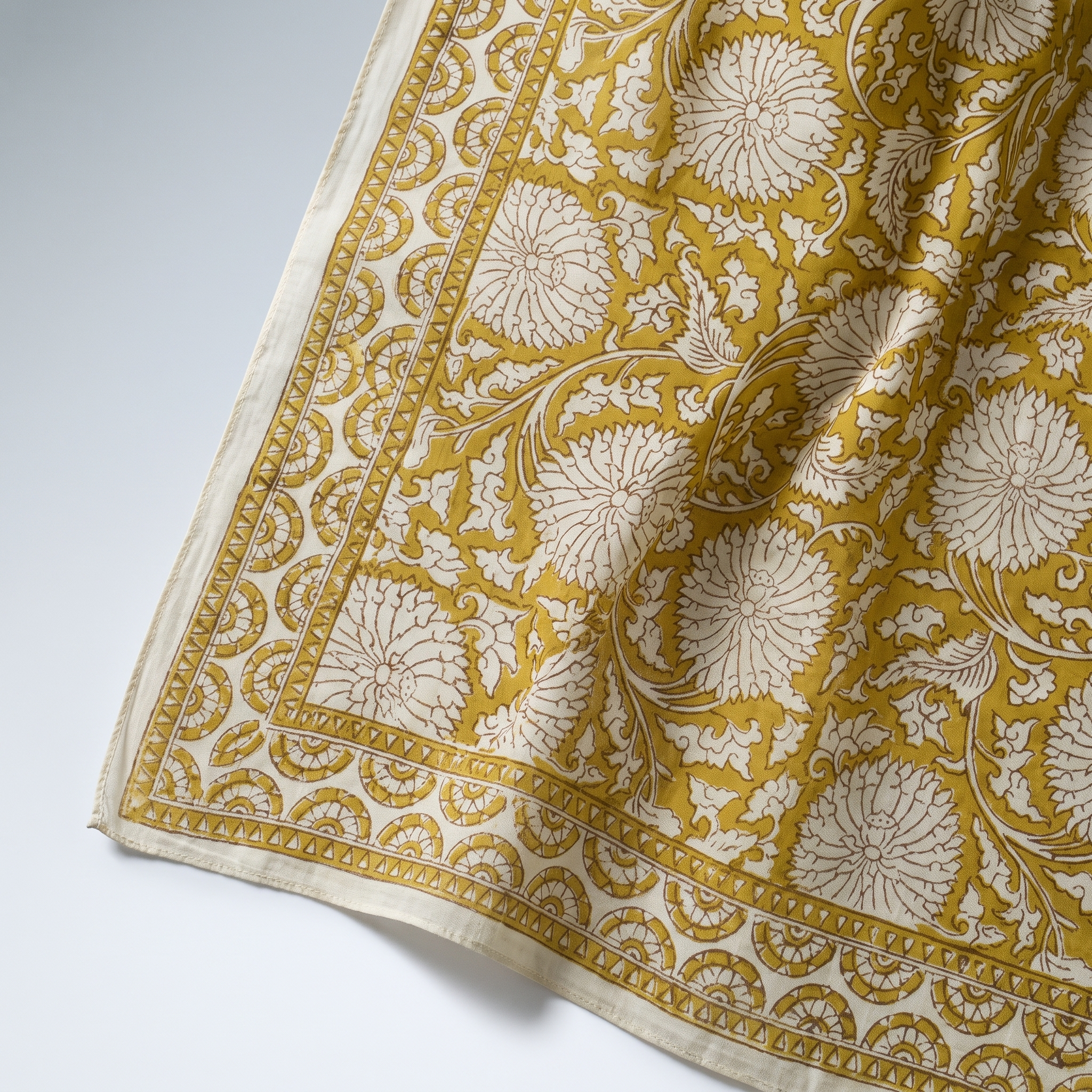Détail du blockprint du paréo Haldi : fleurons crème réservés dans le jaune curcuma, bordure à dents et liseré écru