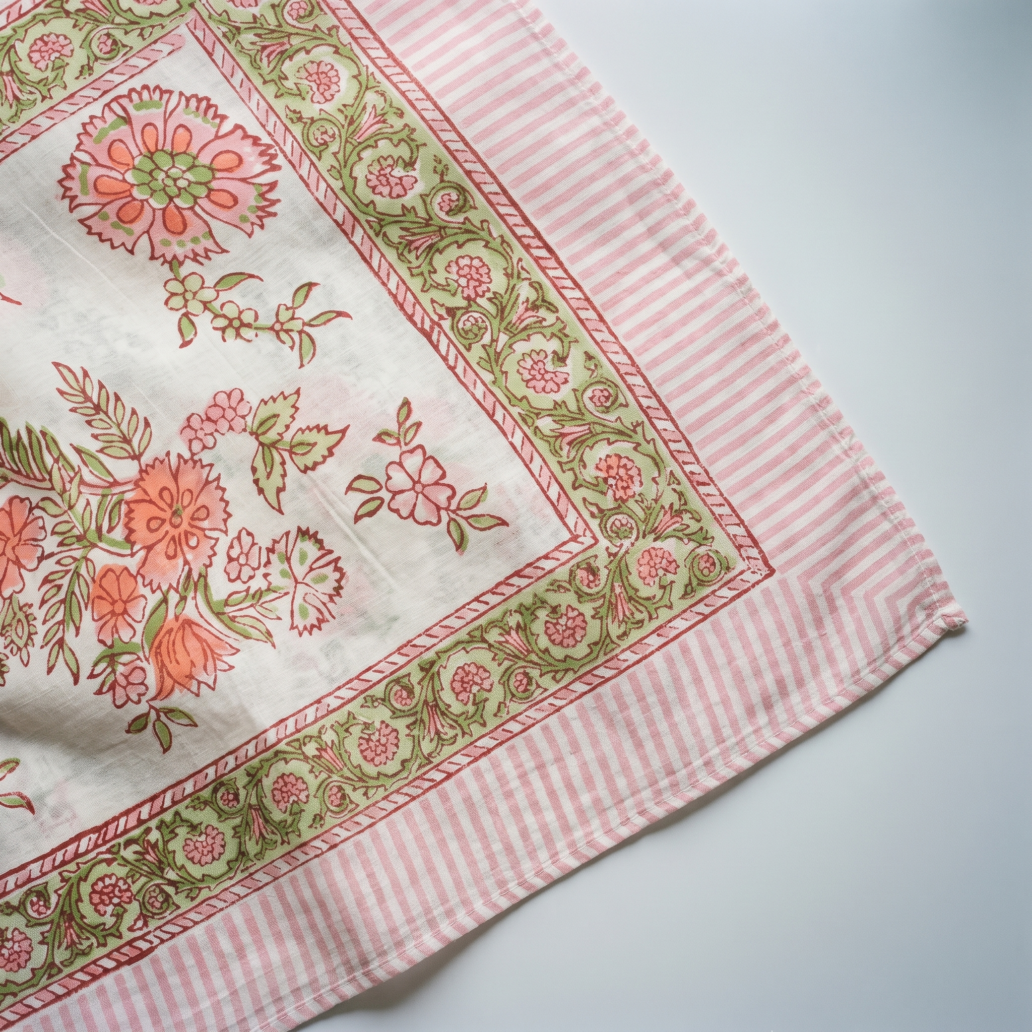 Détail du blockprint du paréo Champa : corolles corail cernées de brique, fougères vert amande et bordure rayée rose