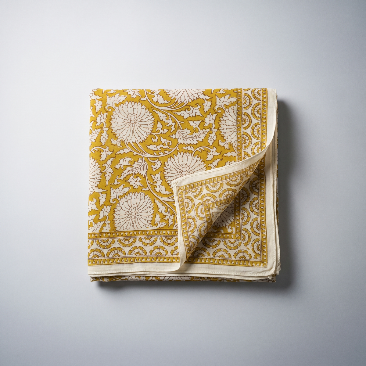 Paréo Haldi plié à plat : coton blockprint, fleurons crème réservés sur jaune curcuma, bordure à dents et liseré écru
