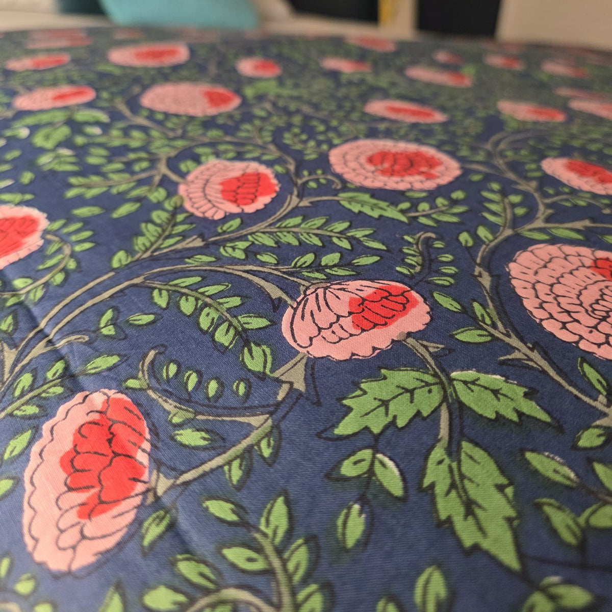Gros plan du blockprint de la housse Nilima : fleurs rose saumon à cœur corail et feuilles vertes sur fond bleu marine