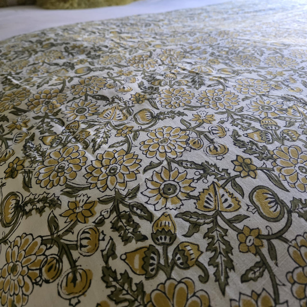 Gros plan du blockprint de la housse Sevanti : fleurs moutarde et feuillage olive cernés de sombre sur coton écru