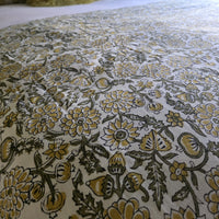 Gros plan du blockprint de la housse Sevanti : fleurs moutarde et feuillage olive cernés de sombre sur coton écru