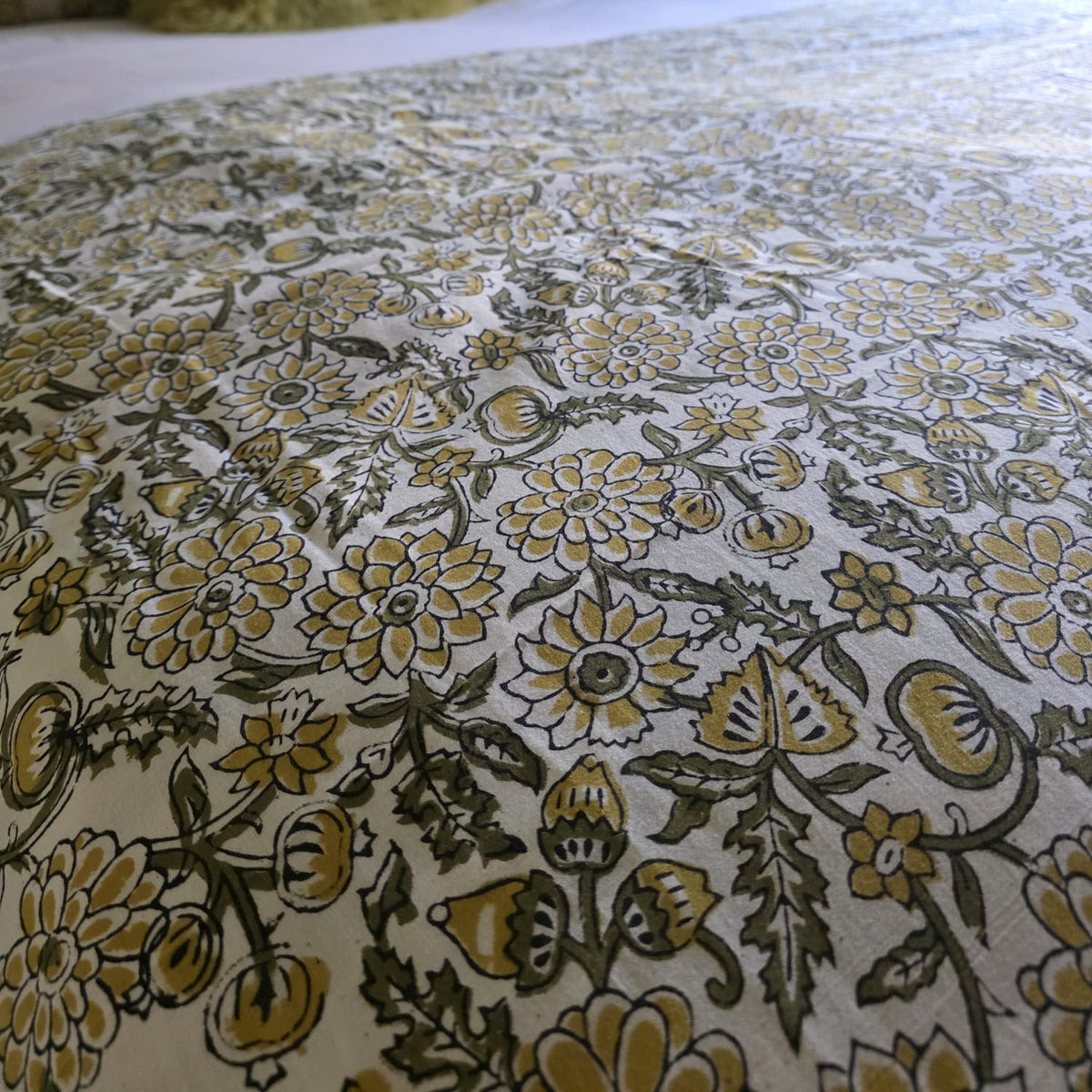 Gros plan du blockprint de la housse Sevanti : fleurs moutarde et feuillage olive cernés de sombre sur coton écru