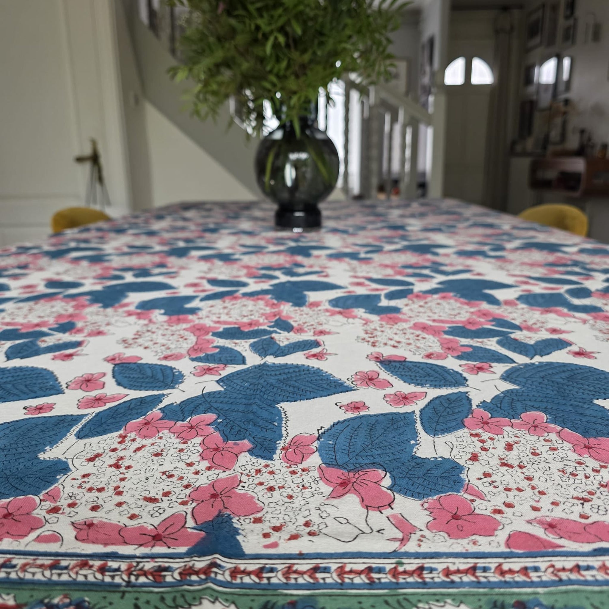 Nappe Anjana dressée sur une table : coton écru imprimé de feuillage indigo et de grappes roses, large bordure verte