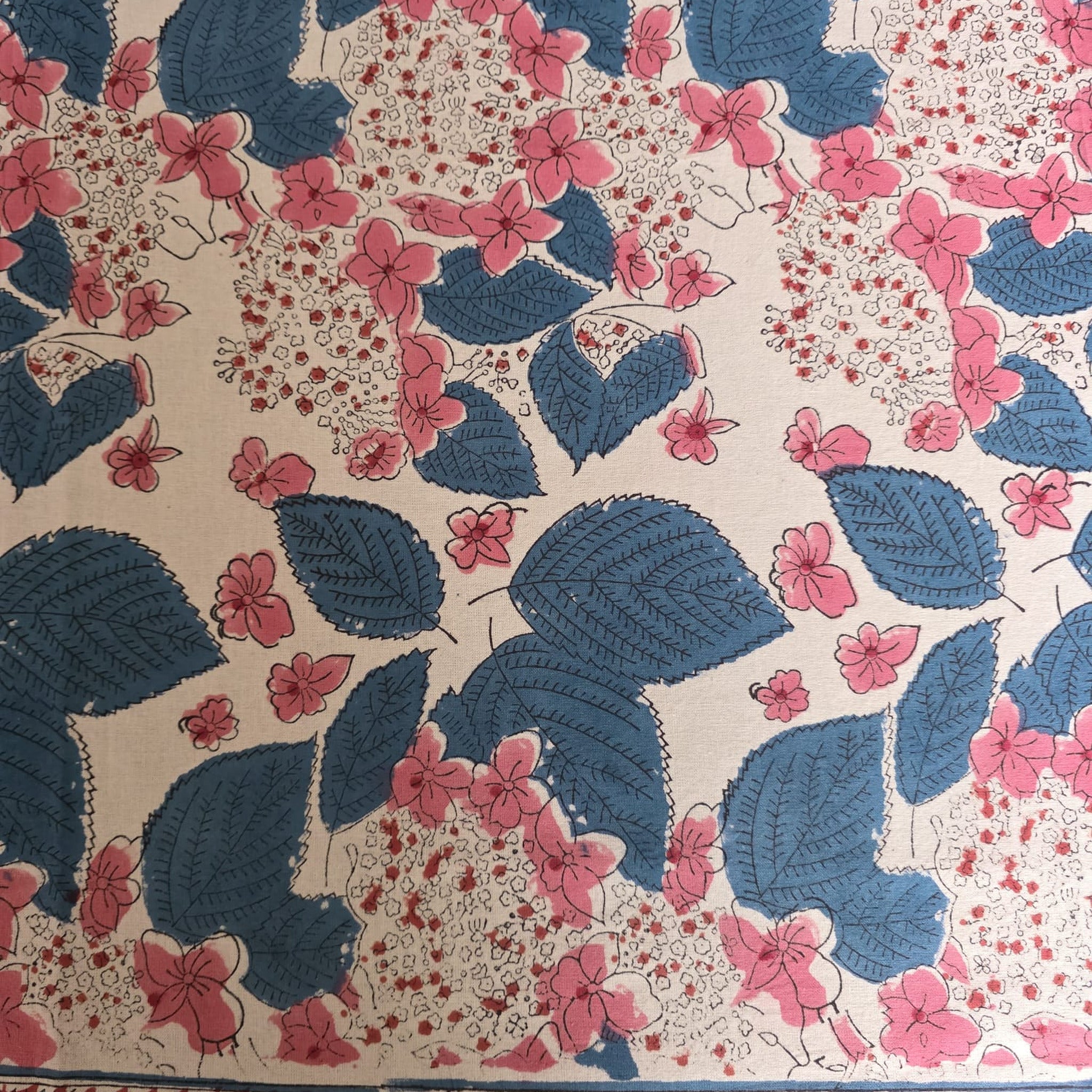 Détail du blockprint de la nappe Anjana : feuilles indigo nervurées et grappes de fleurs roses sur coton écru