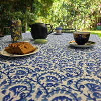 Nappe Lehar dressée sur une table de jardin, motif indigo en arcs sur coton écru, théière noire et gâteau