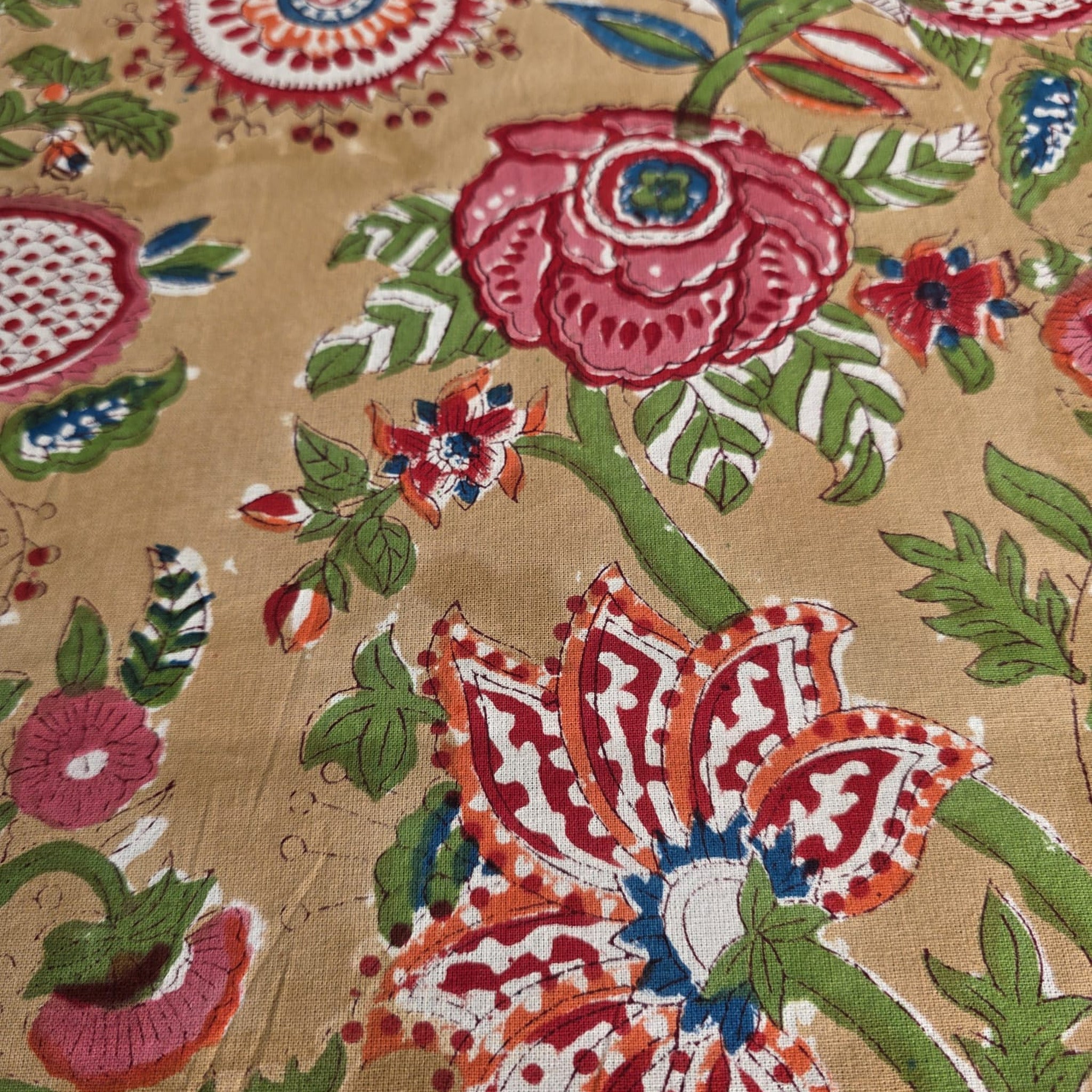 Détail du coton imprimé au bloc de bois : roses framboise et palmettes sur le fond miel de la nappe Madhu