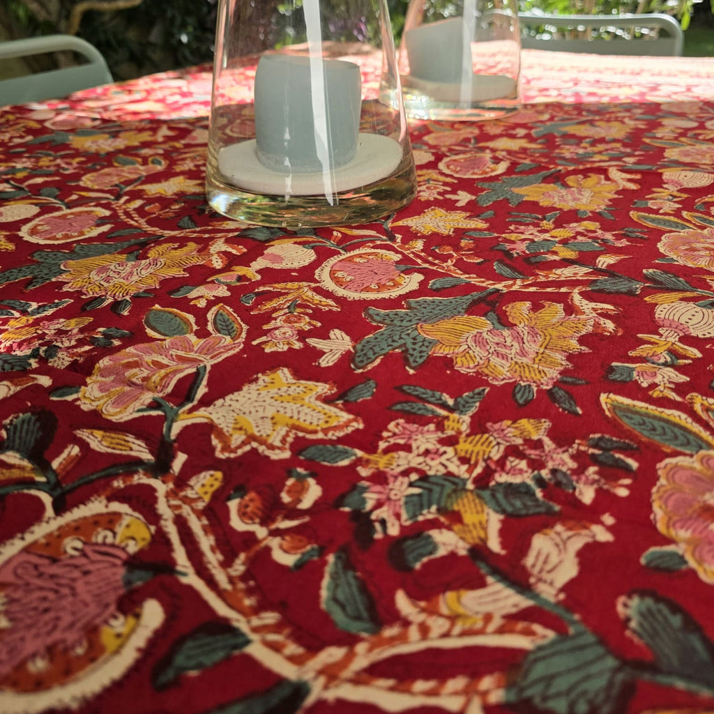 Nappe Manika sur une table de jardin, jardin fleuri crème et safran sur fond rouge profond