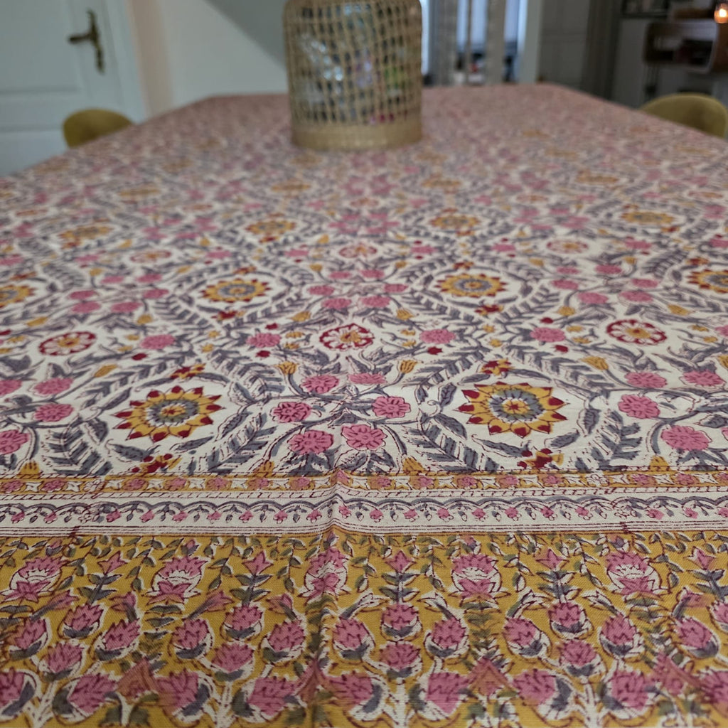 Nappe Suman dressée sur une table : semis de rosaces safran et de fleurs roses sur coton écru, feuillage gris ardoise