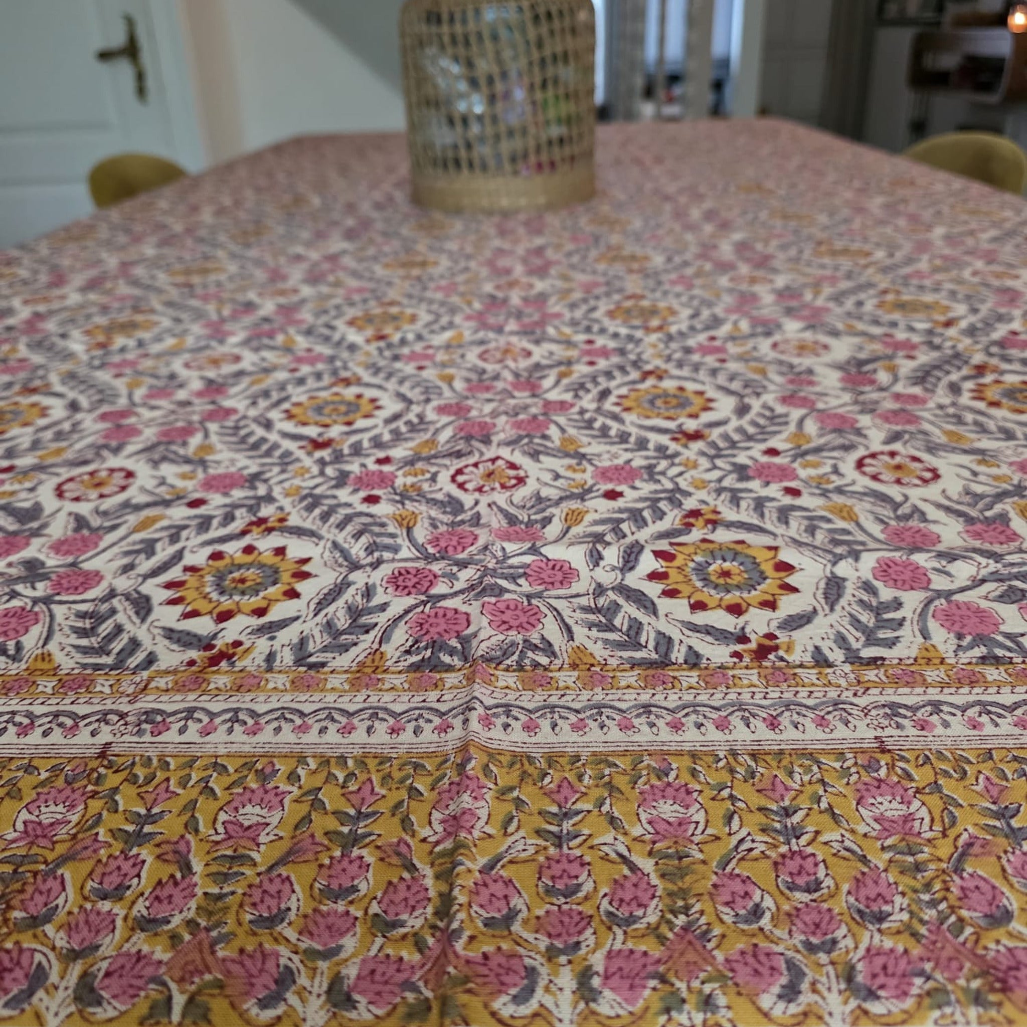 Nappe Suman dressée sur une table : semis de rosaces safran et de fleurs roses sur coton écru, feuillage gris ardoise