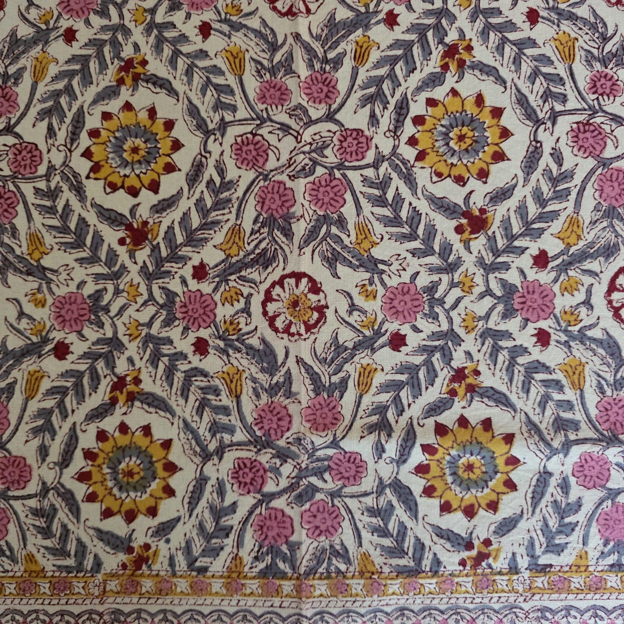 Détail du blockprint de la nappe Suman : rosaces safran à cœur rouge, fleurettes roses et feuilles ardoise