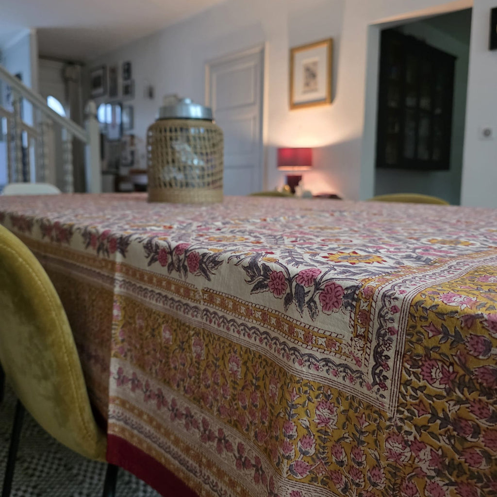 Nappe Suman sur la table d’une salle à manger claire, retombée et bordure fleurie visibles